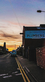 Road sign on street against sky at sunset