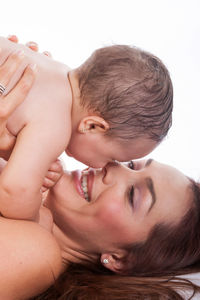 Happy mother playing with shirtless daughter while lifting her against white background