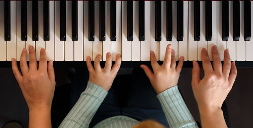 Cropped hand of mother and daughter playing piano at home