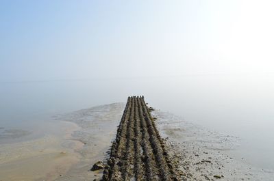 Tire tracks on wet sand amidst sea against sky