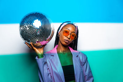 Portrait of woman wearing sunglasses standing against blue wall