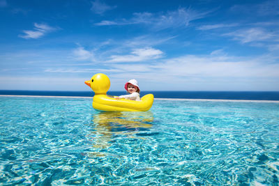 Baby girl with inflatable ring on infinity pool against blue sky