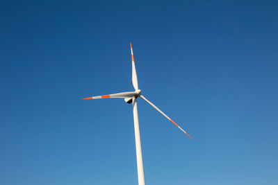 Low angle view of wind turbine against clear blue sky