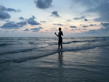 Rear view of man standing at beach during sunset