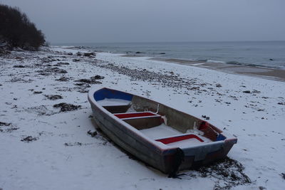 Boat moored on shore against sky during winter