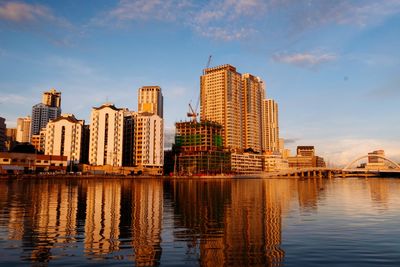 Buildings by river against sky during sunset