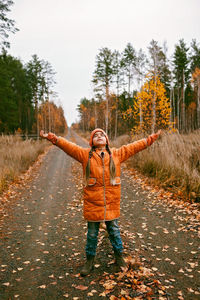 Girl in orange coat with outstretched arms enjoys fresh air in fall forest. mental health, autumn