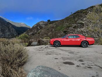 Red car on road by mountains against sky