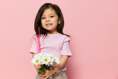 Portrait of young woman holding flowers against pink background
