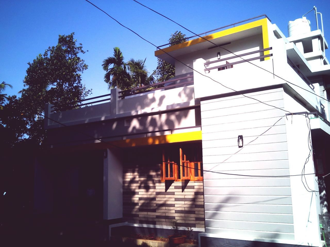 architecture, built structure, building exterior, low angle view, power line, clear sky, house, residential building, residential structure, sky, cable, window, building, electricity, outdoors, sunlight, no people, day, city, blue