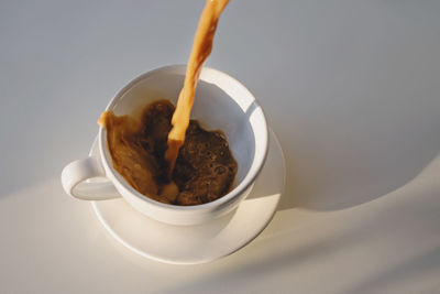 Pouring of coffee in a cup creating splash. morning, minimalist concept