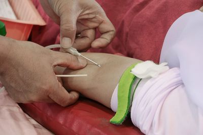 Cropped hands of doctor inserting iv drip on patient hand in hospital