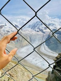 Cropped hand holding chainlink fence against landscape