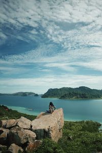 Man sitting on rock by mountain against sky