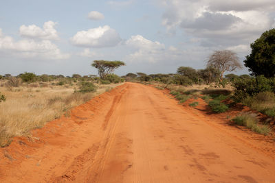 Dirt road passing through landscape against sky