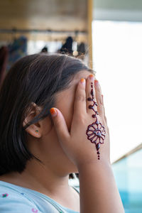 Portrait of henna ornaments on young girl's hand covering face.