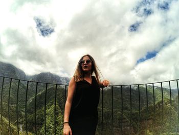 Young woman standing at observation point on mountain against cloudy sky