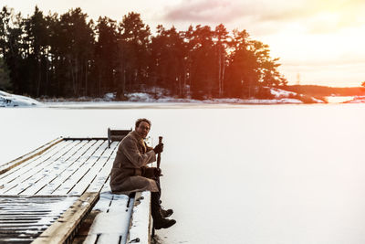 Man sitting on snowy landscape against sky