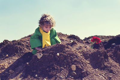 Boy sitting on mud against sky