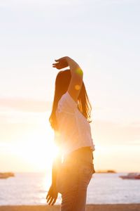 Woman standing at beach against sky during sunset