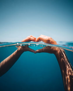 Close-up of hand against sea against clear blue sky