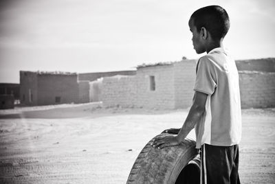 Side view of boy with tire standing on field against sky