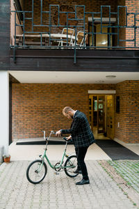 Side view of man with bicycle standing by building in city