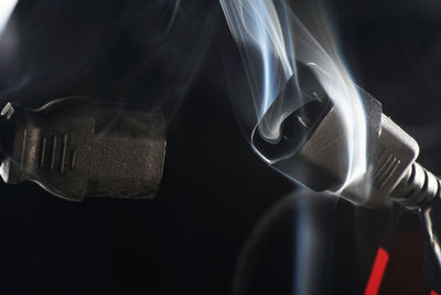 Close up of smoke emitting from electric plugs against black background