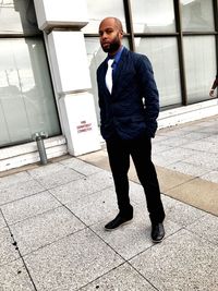 Portrait of businessman with hands in pockets standing on sidewalk by building