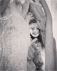 Portrait of smiling young woman against tree trunk