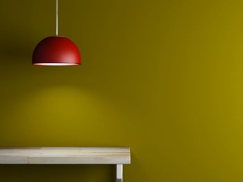 Illuminated red pendant light hanging over wooden table by yellow wall