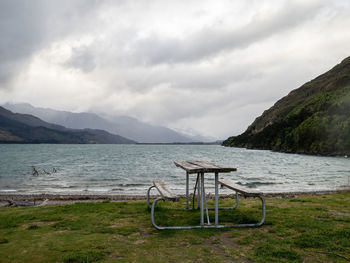 Scenic view of sea and mountains against sky, picnic table in foreground