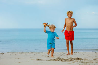 Full length of shirtless man standing at beach against sky