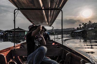 Woman sitting on boat against sky during sunset