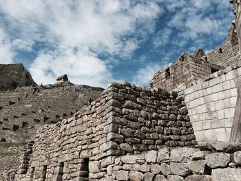 Low angle view of stone wall against cloudy sky