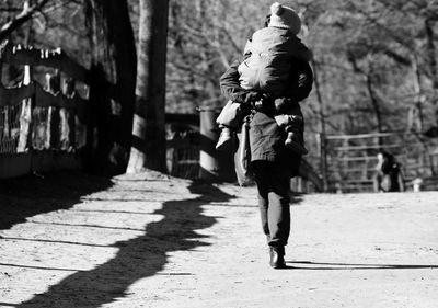 Mother carrying child while walking on road in sunny day