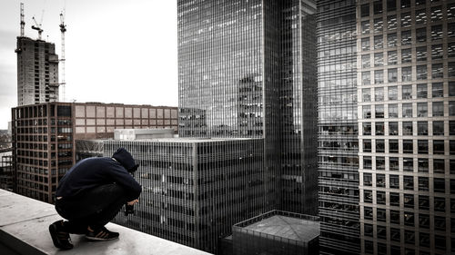 Side view of young man photographing while crouching on building terrace