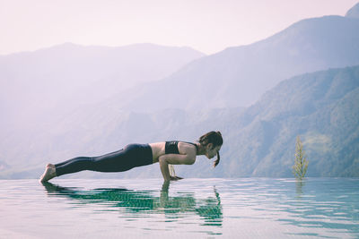 Side view of woman exercising on infinity pool against mountains