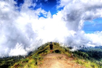 Rear view of man standing on field against cloudy sky