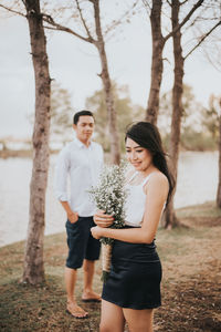 Woman holding bouquet while boyfriend standing on land