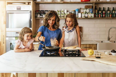 Smiling mother and daughters preparing food in kitchen at home