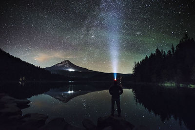 Silhouette man wearing headlamp standing at lakeshore against starry sky