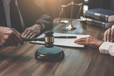 Midsection of lawyer banging gavel with woman in courtroom