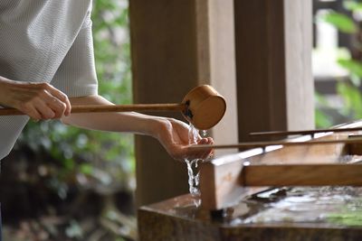 Midsection of woman washing hand with water in shrine