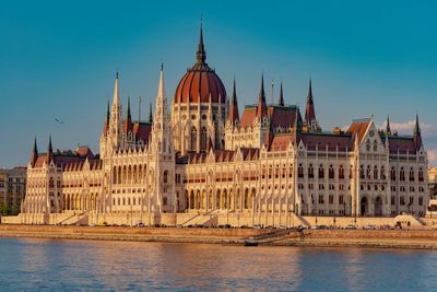 Hungarian parliament building by river against blue sky