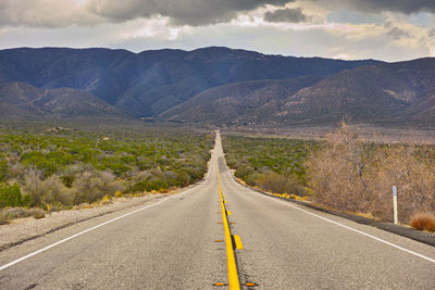 Empty road by mountains against sky