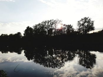 Silhouette trees by lake against sky