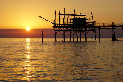 Silhouette built structure on sea against sky during sunset