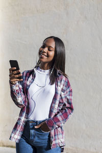 Young woman using phone while standing on wall