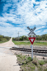 Road sign by railroad tracks against sky